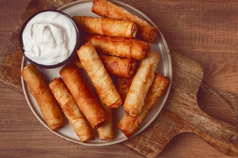 Fried spring rolls with cheese, on a wooden background, with cream sauce, no people
