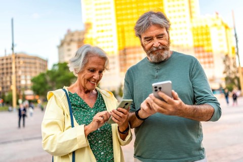 Happy caucasian casual senior couple using phone standing in an urban square