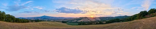 Typical Tuscan landscape in Val d'Orcia with hills, trees, fields, cypresses and farm road in