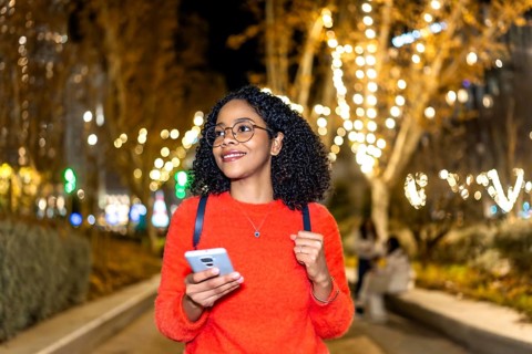 Smiling student walking in a decorated city using her smartphone during christmas holidays