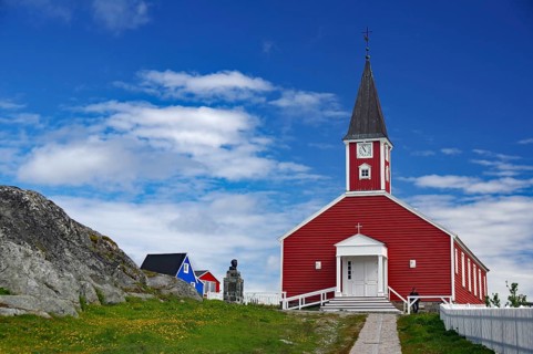 Red church with white entrance and tower, sculpture next door under a blue sky, Church of the