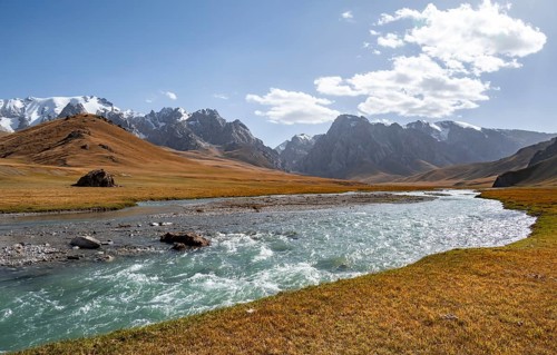 Mountain landscape with yellow meadows and river Kol Suu, mountain peak with glacier, hike to the