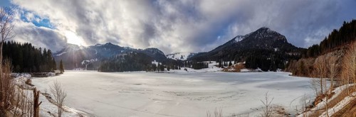 Snowy winter landscape with mountains, densely wooded slopes and partly cloudy skies, Spitzingsee