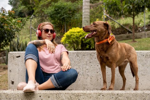 A tranquil woman with headphones sits in the plaza accompanied by her faithful pet