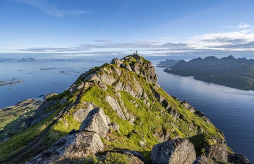 Climber on the summit of Dronningsvarden or Stortinden, behind sea and fjord Umvågsundet,