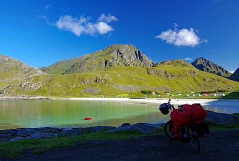View of a bicycle with red bags on the shore of a bay, surrounded by green hills and mountains