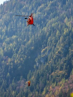 2 mountain rescuers of the Bavarian Mountain Rescue Service are winched by the on-board mechanic of