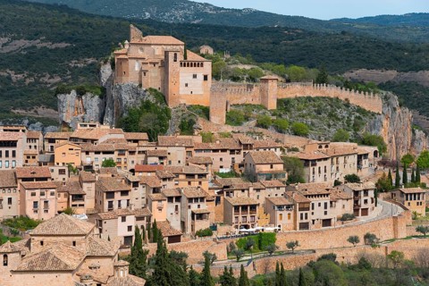 Historic castle overlooking a medieval village, surrounded by green countryside and mountains,