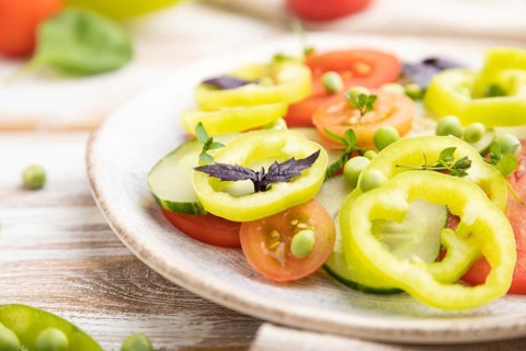 Vegetarian salad from green pea, tomatoes, pepper and basil on white wooden background and linen
