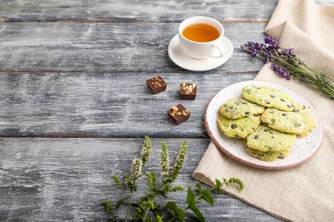 Green cookies with chocolate and mint on ceramic plate with cup of green tea and linen textile on