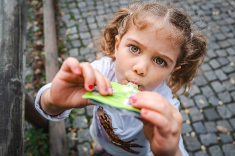 A young girl with pigtails eats a snack on a cobbled street and looks curiously, Stuttgart,