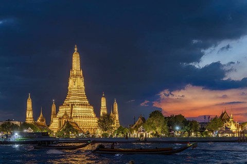 Wat Arun, Temple of Dawn at sunset with dark clouds. Boats on the Chao Phraya river. Tourist