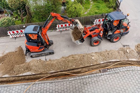 Construction workers laying fibre optic cable in trench under asphalt, cable trench, excavator,