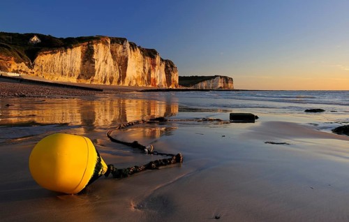 Chalk cliffs of the Alabaster Coast in the evening light, in front a yellow buoy on the beach at