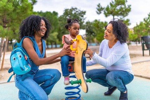 African mother and grandmother holding a girl on a swing in the playground