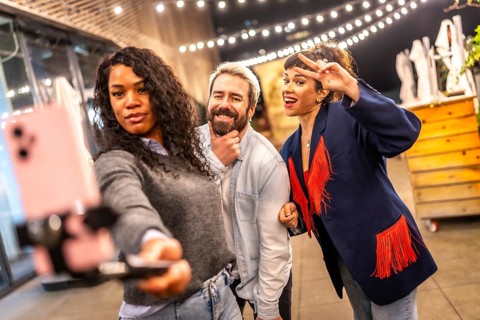 Friends gesturing success while streaming online video with smartphone during party at night