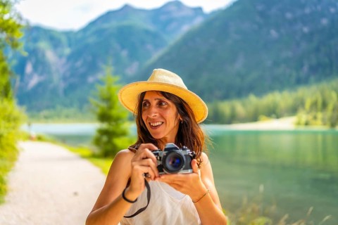 Smiling tourist with straw hat taking photos at lake dobbiaco in the dolomites during summer