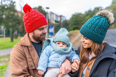 Parents holding their baby while enjoying a leisurely stroll in a park during wintertime, creating