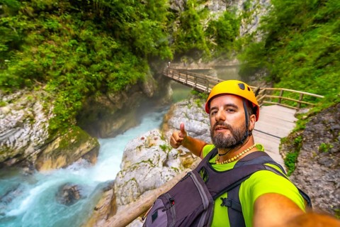 Tourist wearing helmet and backpack hiking in vintgar gorge, near bled, slovenia, making thumbs up