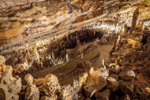 Tourists walking on illuminated footpath inside the famous postojna cave, a karst cave system near