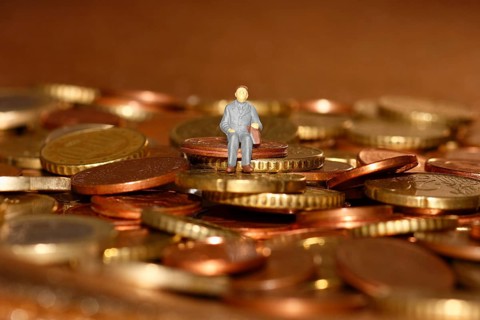 Miniature man sitting among euro coins, North Rhine-Westphalia, Germany, Europe