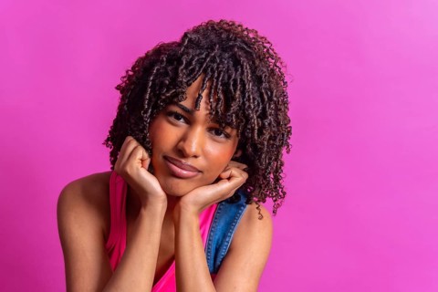 Portrait of a thoughtful young woman with curly hair resting her chin on her hands against a