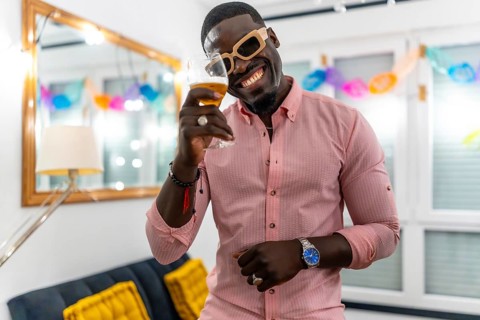 African man wearing sunglasses smiling and toasting at camera during a home party