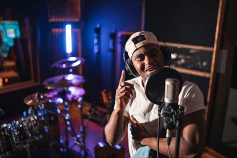 Young black man recording vocals for new album in professional music studio, wearing headphones and