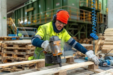 Man with protective gear repairing pallets in a recycling plant warehouse using a compressed air
