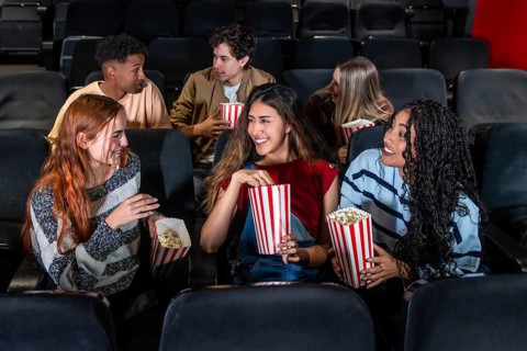 Cheerful multi ethnic friends enjoying popcorn while watching a film together in a cozy movie