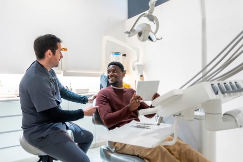 Dentist shows the results of a dental checkup to a smiling patient on a tablet in a modern, bright