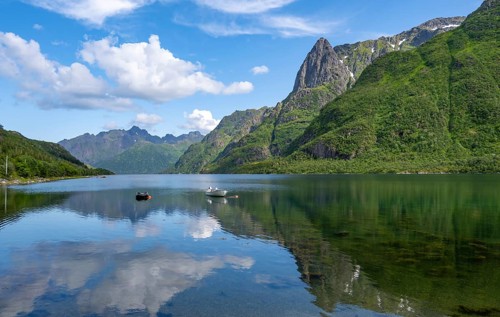 Small boats at the fjord Austnesfjorden, idyllic Norwegian fjord landscape, mountains reflected in