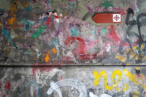 Graffiti-covered concrete wall with Olav's Cross signposting for pilgrims on the Olav Trail or