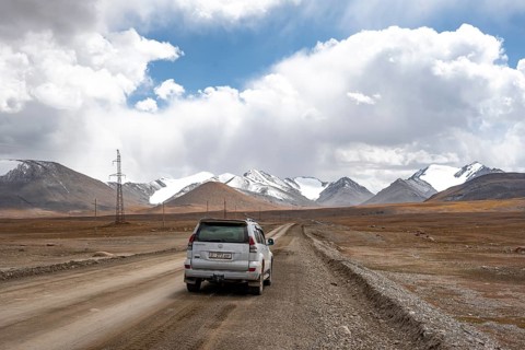 Off-road vehicle on a gravel track, glaciated and snow-covered peaks, Ak Shyrak Mountains, near