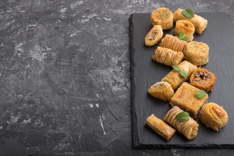 Traditional arabic sweets (kunafa, baklava) on a black slate board on a black concrete background.