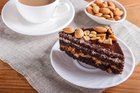 Chocolate cake with caramel, peanuts and almonds on a brown wooden background. cup of coffee, top