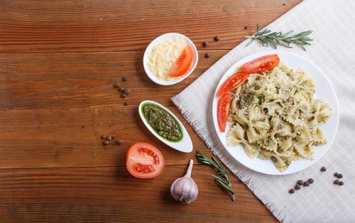 Farfalle pasta with pesto sauce, tomatoes and cheese on a linen tablecloth on brown wooden