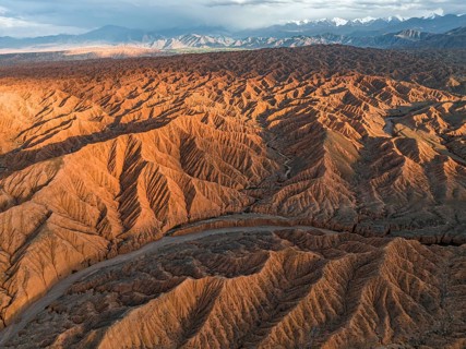 River bed runs through a landscape of eroded hills, badlands at sunset, mountain peaks of the Tian