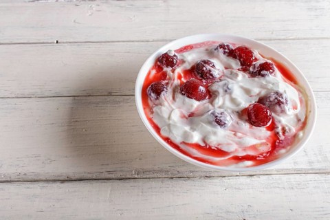 White plate with greek yogurt and strawberry jam on white wooden background. close up. copy space