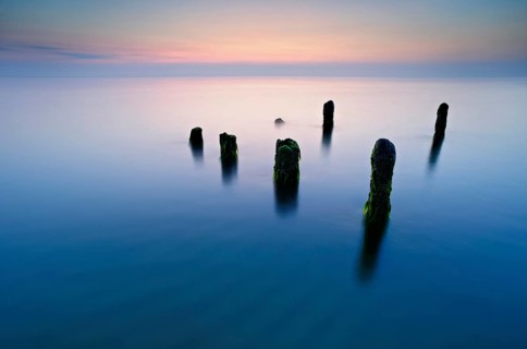 Old posts with algae in the water on the Baltic Sea beach, long exposure at sunset,