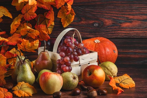 A basket of grapes and plums surrounded by pears, apples, a pumpkin, chestnuts and autumn leaves