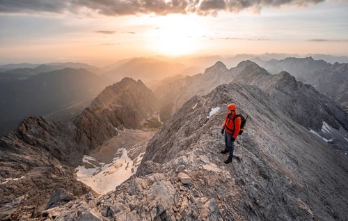 Mountaineer with helmet on a narrow rocky ridge at sunrise, crossing the Jubiläumsgrat, view of