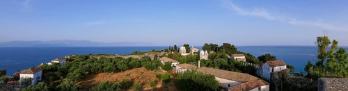 Wide panorama of the whole complex, with church and trees, the sea stretches to the horizon,