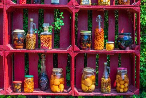 A red wooden shelf with jars and bottles full of pickled fruits and vegetables at the Hortulus
