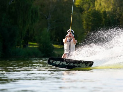 Sporty young man with helmet and waistcoat on wakeboard in lake, water sports, water skiing in