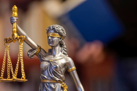 Close-up of a Justitia, in the background a man is reading a book (symbolic image)