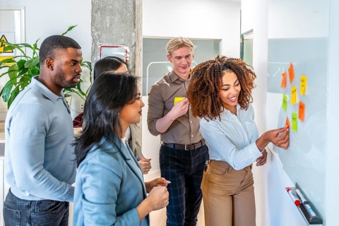 Diverse team collaborating, using sticky notes on a whiteboard during a brainstorming session in a