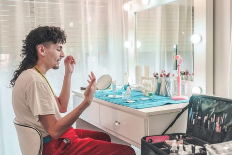 Young male makeup artist applying foundation in front of a mirror at a professional beauty salon,