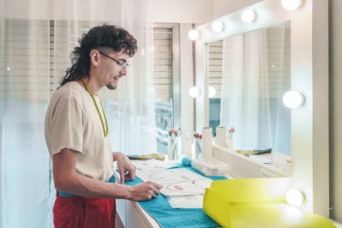 Young male make-up artist carefully reviewing face charts, preparing for diverse clientele in a