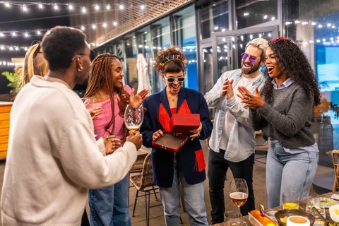 Young multi-ethnic friends giving birthday gift to a woman at night party in the terrace of a bar
